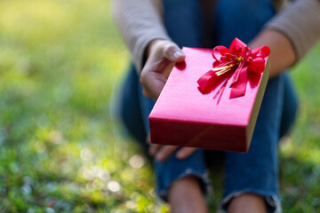 Closeup image of a woman holding and giving a red gift box