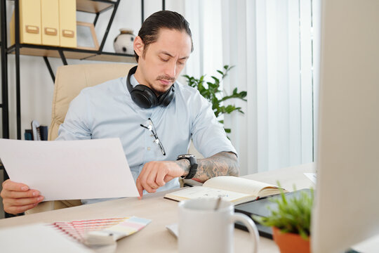 Frowning mixed-race graphic designer checking time on his wrist watch when getting ready for online meeting with client