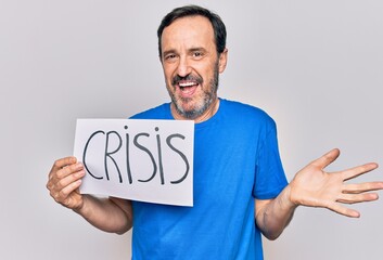 Middle age handsome man holding paper with crisis message over isolated white background celebrating achievement with happy smile and winner expression with raised hand