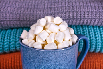 Fototapeta na wymiar Cocoa drink with marshmallows in a blue cup on a knitted background.