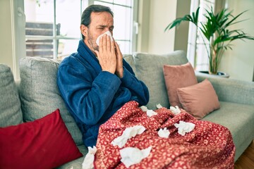Middle age man feeling sick with cold and fever at home, ill with flu disease sitting on the sofa