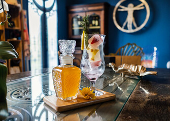 Cocktail glass with ice cubes and decanter with peach tea on wooden tray at cafe.