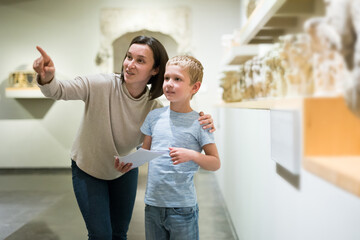Young woman with son observing with interest sculptures exhibition in art museum, pointing to something interesting