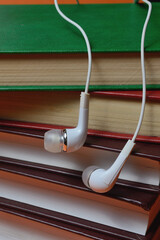 small white headphones from the phone lie on a stack of books on an orange background.