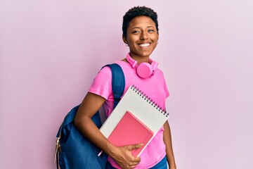 Young african american girl wearing school bag and holding books looking positive and happy...