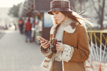 Beautiful girl in a brown jacket. Woman in a spring city. Lady with mobile phone.