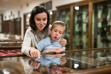 Young woman with son observing with interest exhibition under glass in art gallery