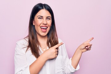 Young beautiful brunette woman wearing elegant shirt standing over isolated pink background smiling and looking at the camera pointing with two hands and fingers to the side.