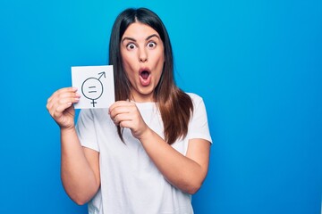 Young beautiful woman asking for sex discrimination holding paper with gender equality concept scared and amazed with open mouth for surprise, disbelief face