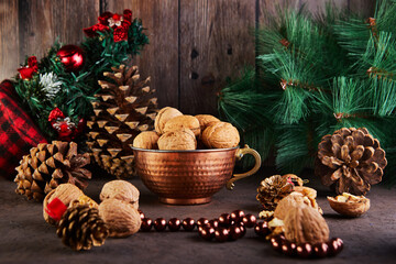 Fototapeta na wymiar Walnuts in a tin cup, whole and chopped, next to the filling and shells. Presented in a New Year's composition with fir cones. Home storage of winter preparations