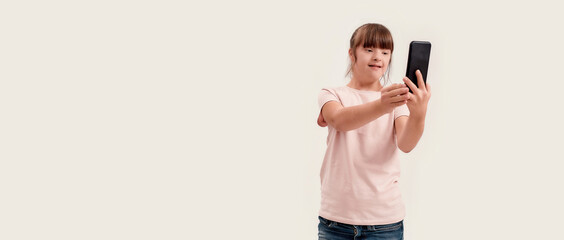 Portrait of disabled girl with Down syndrome using smartphone while taking selfie picture, standing...