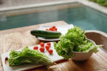  Fresh vegetables - cherry tomatoes, lettuce and cucumber on the cutting board at home kitchen. The concept of vegeterian food