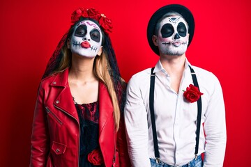 Couple wearing day of the dead costume over red looking at the camera blowing a kiss on air being lovely and sexy. love expression.