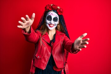 Woman wearing day of the dead costume over red looking at the camera smiling with open arms for hug. cheerful expression embracing happiness.