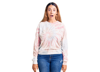 Fototapeta premium Beautiful young woman wearing casual tie dye sweatshirt scared and amazed with open mouth for surprise, disbelief face