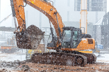 The big excavator is digging in snowy weather.