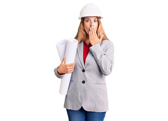 Beautiful young woman wearing architect hardhat holding build project covering mouth with hand, shocked and afraid for mistake. surprised expression