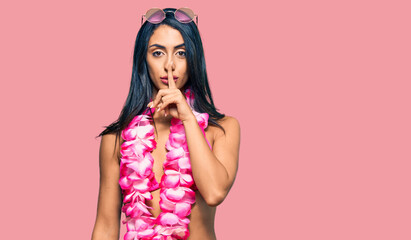 Beautiful hispanic woman wearing bikini and hawaiian lei asking to be quiet with finger on lips....