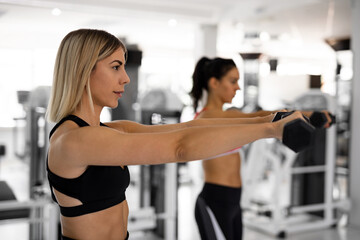 Fototapeta na wymiar Two beautiful women are exercising in the gym with dumbells