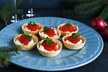 Tartlets with cream cheese and red caviar on a beautiful plate on the New Year's table. New Year's snack.