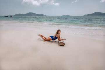 Young attractive blonde woman in a blue swimming suit lying on a sandy beach against the sea background. Summer vacation concept