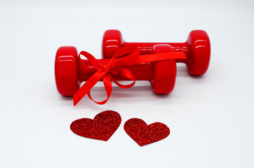 Two red dumbbells with a ribbon bow and two hearts on a white background. Concept of Valentines day, healthy lifestyle, giving gifts, love of sports.