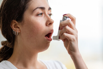 Bronchial asthma. Close-up portrait of a young woman holding an inhaler to her mouth. Blurry...
