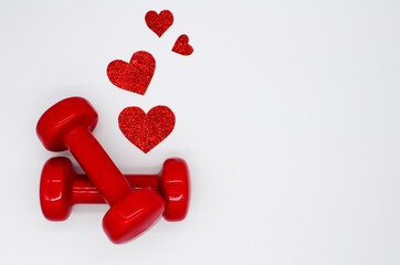 Two red dumbbells and hearts on a white background with copy space. Concept of Valentines day, healthy lifestyle, giving gifts, love of sports, shopping