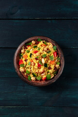 Vegetarian couscous salad with vegetables and herbs, overhead shot on a dark blue wooden background with a place for text