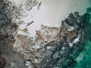 From above photo of a pretty young woman in a blue swimming suit lying on the rock in high tide. Summer vacation concept