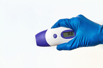 A hand in a protective glove holds an electronic non-contact thermometer. Temperature Measurement...