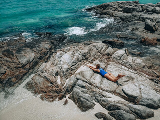 Fototapeta na wymiar Pretty young woman in a blue swimming suit lying on the rocks in high tide. Summer vacation concept