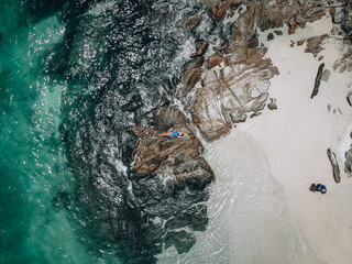 From above photo of a pretty young woman in a blue swimming suit lying on the rock in high tide....