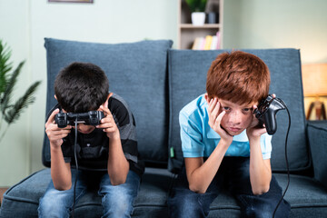 Young kids feeling sad due to lost in videogame while playing at home on sofa - concept of frustration or sadness due to failure in game during childhood.