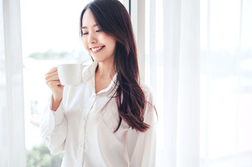 Happy asian woman hands holding coffee cup morning in white bedroom.
