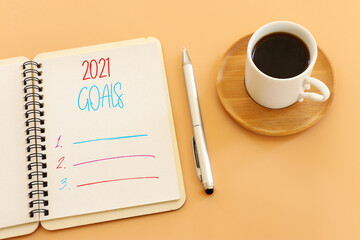 Business concept of top view 2021 goals list with notebook, cup of coffee over pastel yellow background