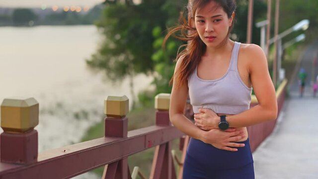 Asian female runner feeling stomachache while running up on the bridge