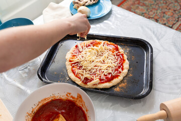 A woman's hand sprinkles cheese on a pizza tray. Close-up view from above. Home cooking