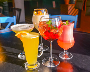 Cocktails on the table. Different coloured drinks in different glasses on dark wooden table.