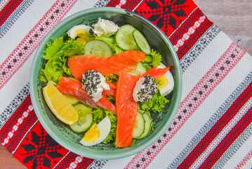 Close up of smoked salmon salad with boiled eggs, cucumbers, cream cheese with sesame seeds and a piece of lemon.