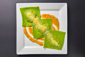 Green ravioli with spinach and meat inside and parmesan cheese on top served in white square plate. Italian cuisine.