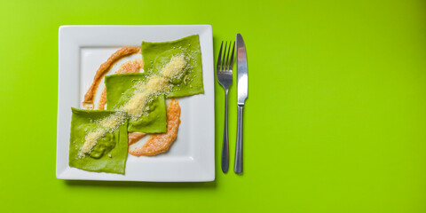 Green ravioli with spinach and meat inside and parmesan cheese on top served in white square plate. Italian cuisine.
