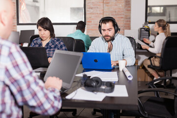 Fototapeta na wymiar Latin hipster guy attentively watching webinar online using headset in modern coworking space