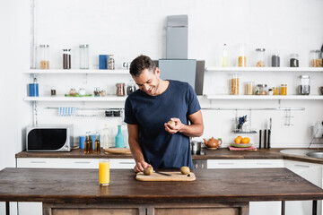  man looking at kiwi on cutting board near orange juice in glass on table in kitchen