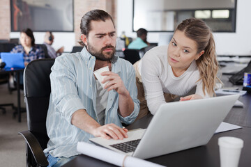 Attractive girl helping Hispanic male colleague in work in modern coworking space