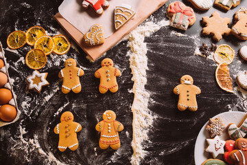 Pandemic cookies. Festive conceptual bakery. Social distancing. Decorated gingerbread man in protective mask divided from biscuits flour powder line on black desk.