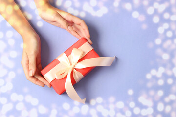 gift in female hands on a colored background top view with golden bokeh and place to insert text