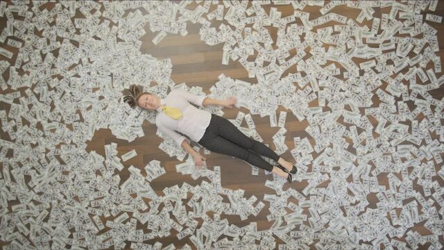 Happy businesswoman rejoice at business success lying in money posing angel on floor in office.