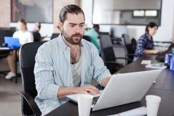 Focused bearded freelancer concentrated on work with laptop in coworking space with international team