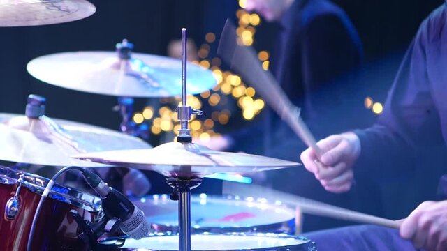 close-up of a rock band drummer playing drums at a concert in a nightclub
hands with drumsticks playing drums in the foreground hi-hat